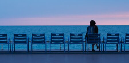 Una persona di spalle seduta guardando un tramonto sul mare.