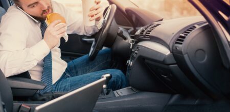 Man eating an hamburger and working seated in his car