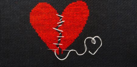 Two halves heart sewn with black thread (iStock/Natalija Grigel)