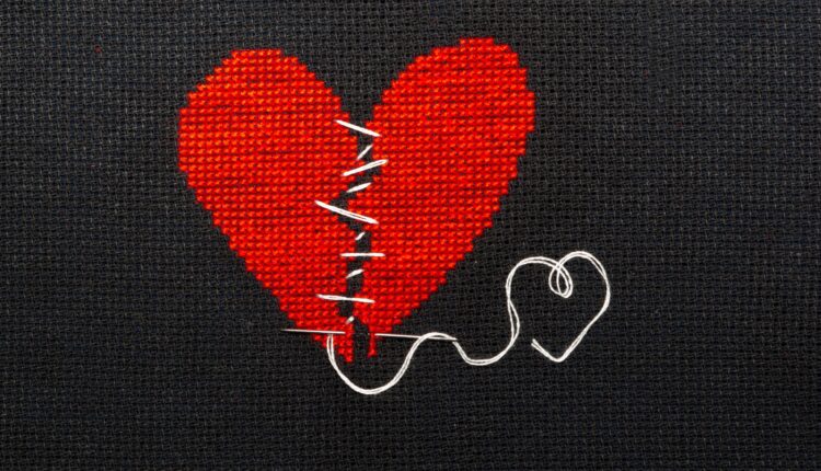 Two halves heart sewn with black thread (iStock/Natalija Grigel)