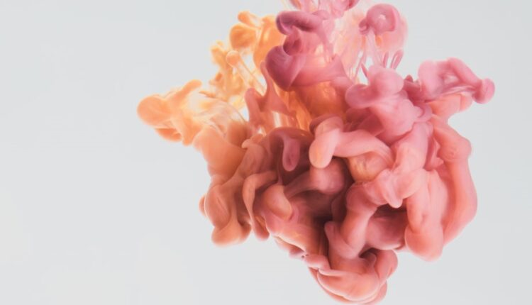 Una goccia di vernice rosa e gialla nell’acqua.