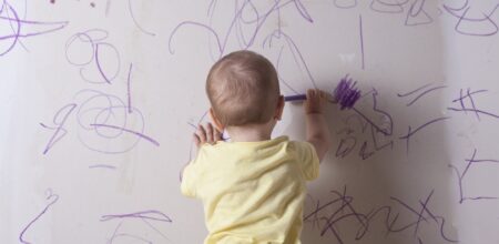 Un bambino scarabocchia un muro.