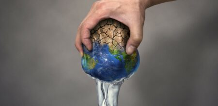 Una mano umana strizza il pianeta Terra, consumando tutta l’acqua.