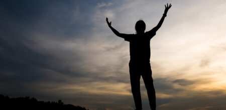 Una persona prega alzando le braccia al cielo