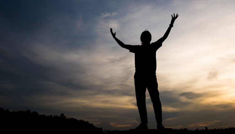 Una persona prega alzando le braccia al cielo